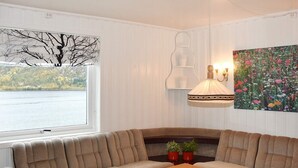 A cozy living room with a large window, a wooden table, a sofa, and a wall-mounted lamp. - 8 Person Holiday Home in Snillfjord (Orkland)
