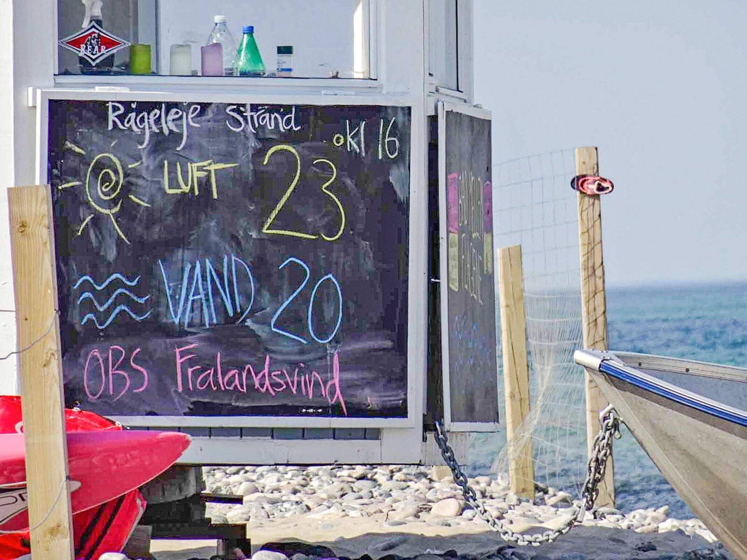 A chalkboard with weather information, including wind direction and speed, and a beachside setting with a boat and surfboards.