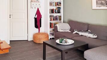 Una sala de estar acogedora con un sofá marrón oscuro, una mesa de centro con bebidas, una estantería y un armario blanco.