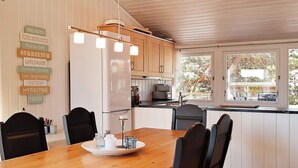 A modern kitchen with white cabinets, a wooden dining table with chairs, and a window overlooking a tree. - 4 Star Holiday Home in Sondeled (Risør)