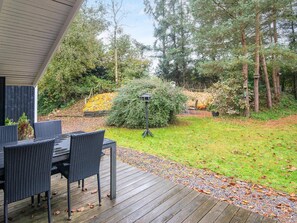A wooden deck with outdoor furniture, surrounded by a garden with trees and a hedge. - 6 Person Holiday Home in Ansager (Ansager)