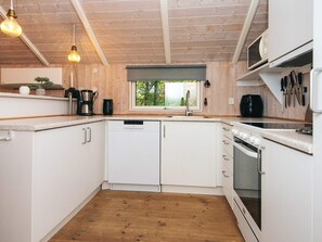 A modern kitchen with white cabinetry, a built-in oven, and a window overlooking greenery. - 6 Person Holiday Home in Ansager (Ansager)