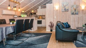 Ett modernt kök med matplats, med bland annat ett träpanelat tak, hängande lampor och en soffa med ett geometriskt mönstrat kuddöverdrag.