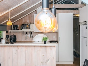 Cocina compacta con muebles de madera, un refrigerador blanco, microondas y una lámpara colgante.