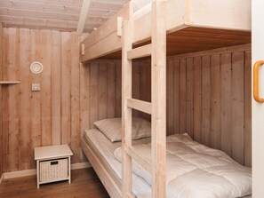 A wooden bunk bed room with a small white nightstand and a wicker basket.