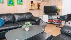 A modern living room with a black leather sofa, a small round table with a plant, and a television on a white cabinet. - 6 Person Holiday Home in Ansager (Ansager)