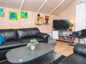 A modern living room with a black leather sofa, a small round table with a plant, and a television on a white cabinet. - 6 Person Holiday Home in Ansager (Ansager)