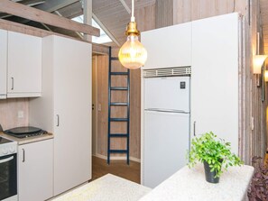 A kitchen with white cabinets, a stainless steel refrigerator, a gas stove, a wooden ladder, and a hanging light fixture. - 6 Person Holiday Home in Ansager (Ansager)