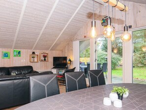 A modern living room with a black leather sofa, a dining table with chairs, and a TV.