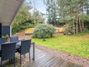 A wooden deck with outdoor furniture, surrounded by a garden with various plants and trees. - 6 Person Holiday Home in Ansager (Ansager)