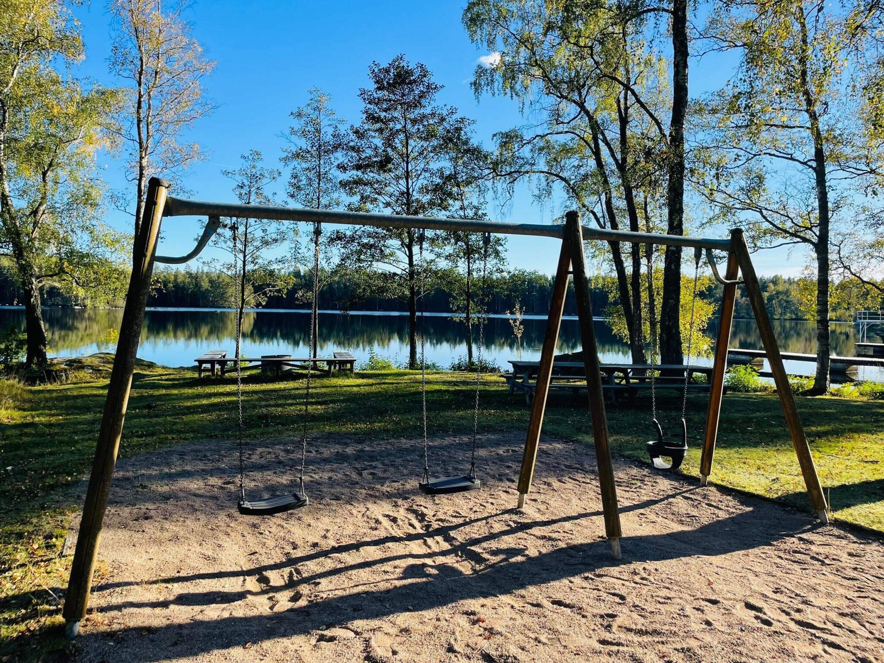 A park with a swing set and picnic tables by a lake.