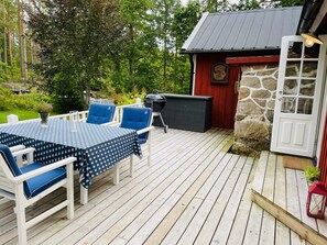 En träaltan med ett bord och stolar, en stenmur och en röd byggnad med en skylt.