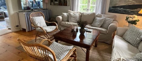 A living room with a wooden floor, a television, a bookshelf, a sofa set, and a painting of a ship.