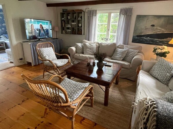Ein Wohnzimmer mit Holzboden, einem Fernseher, einem Bücherregal, einer Sofagarnitur und einem Gemälde eines Schiffes.