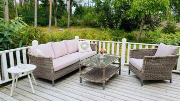 A wooden deck with wicker furniture, including a sofa and two chairs, and a small round table.