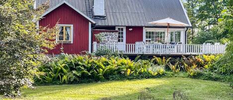 A red house with a stone facade, a white picket fence, and a grassy yard.