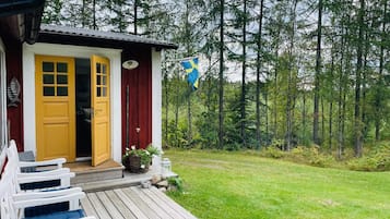 Uma cabana com deck de madeira, porta amarela e uma bandeira azul.