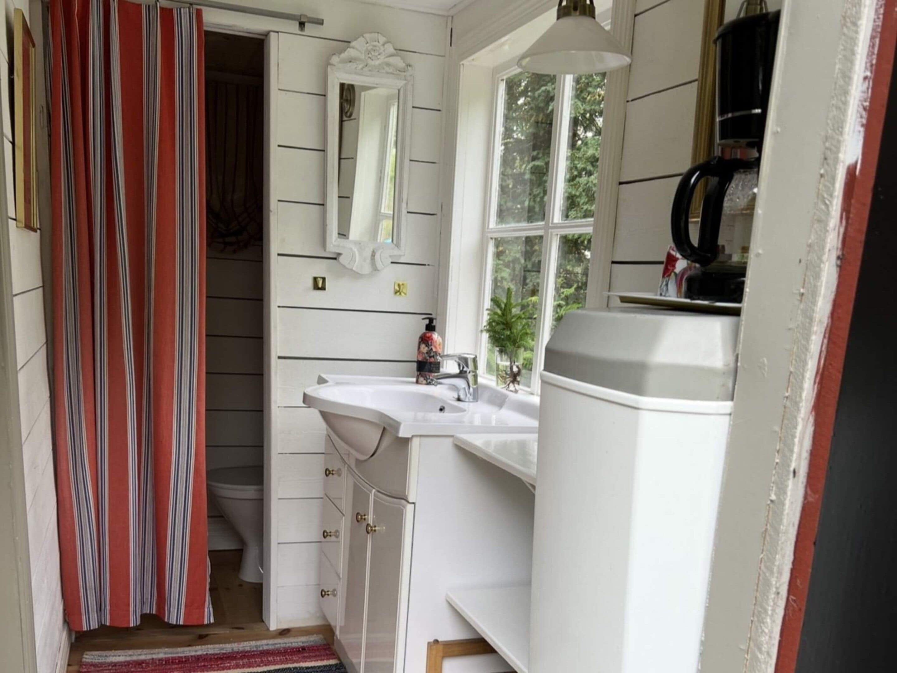 A bathroom with a white sink, a mirror, a window, and a shower curtain.