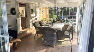 A covered patio with wicker furniture, a table set for dining, and a view of the outdoors.