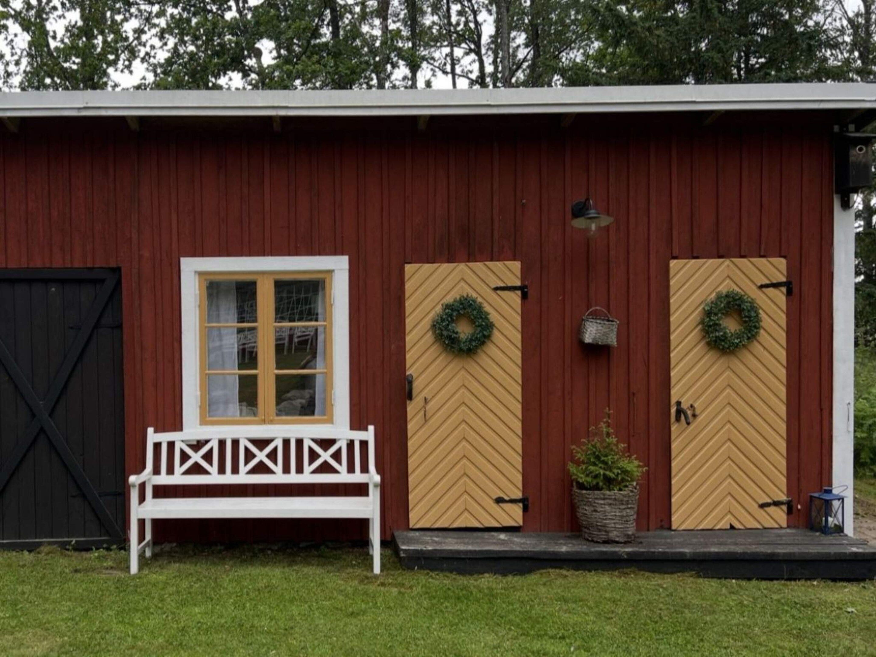 Um edifício vermelho com um banco branco, duas portas decoradas com guirlandas e um portão preto.
