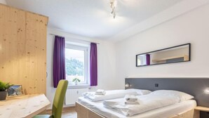 Un dormitorio con una cama de madera, un escritorio, una silla y una ventana con cortinas moradas.