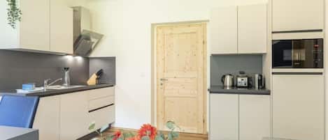A modern kitchen with white cabinets, a wooden door, and a small dining area with a table and a vase of flowers.
