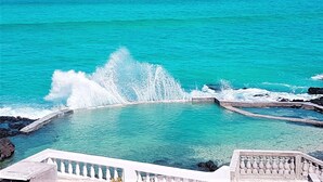 Vista despejada de un océano turquesa con olas rompiendo sobre una costa rocosa.