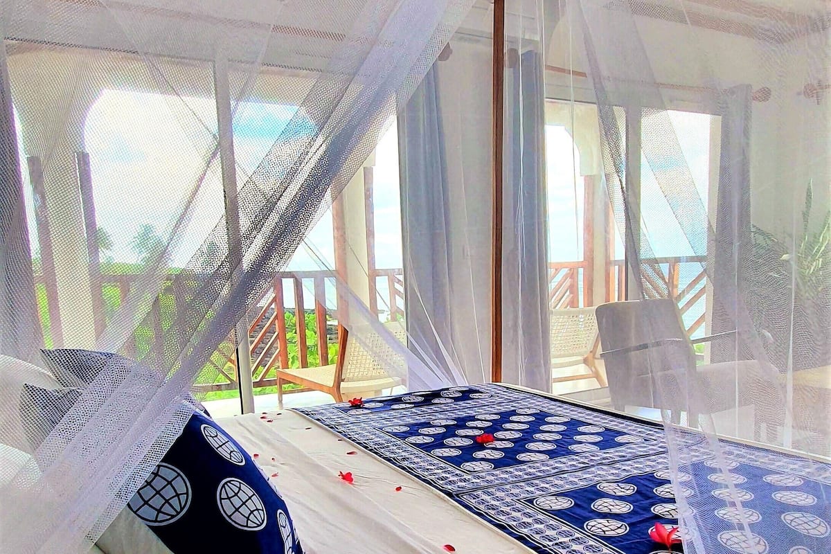 Uma cama com colcha azul e branca estampada, um travesseiro branco e um dossel.