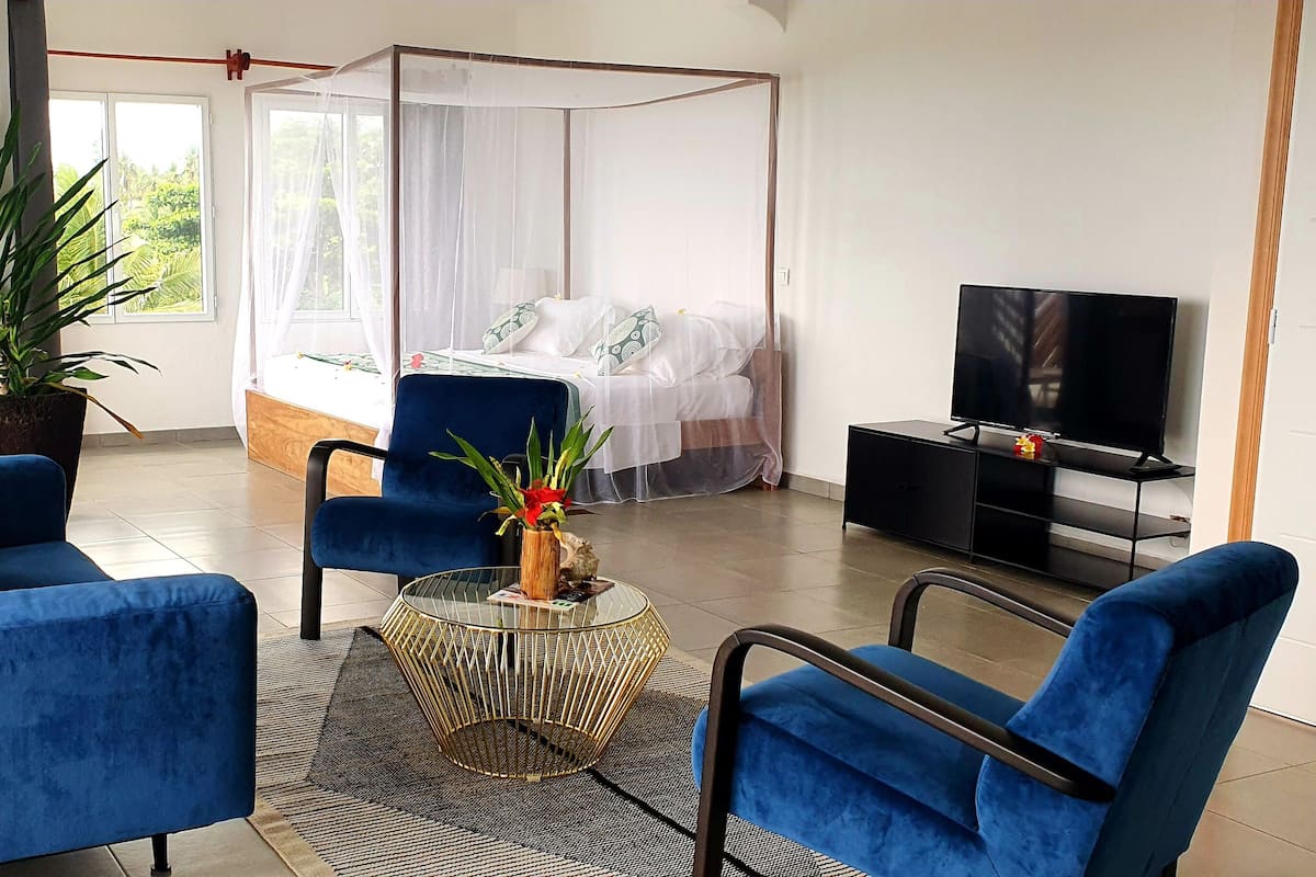 Quarto moderno com cama, televisão e dois sofás azuis.
