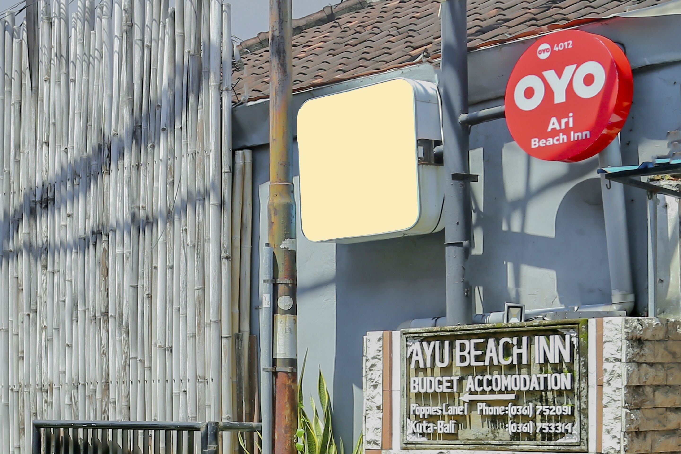 A sign for OYO Ari Beach Inn and a sign for Ayu Beach Inn indicating budget accommodation with contact numbers.