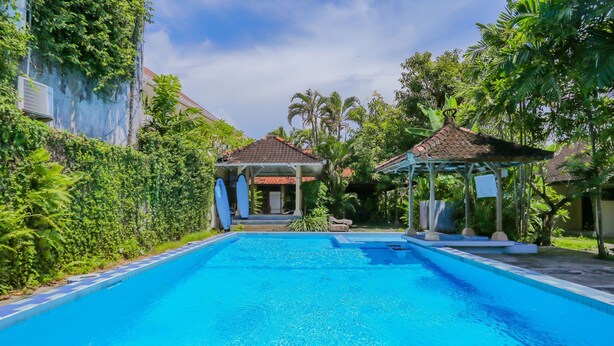 Una piscina con solárium empedrado, rodeada de abundante vegetación y dos gazebos.