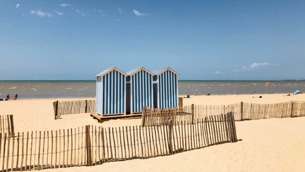 Ein Strand mit zwei Streifen-Strandkörben und einem Holzzaun.