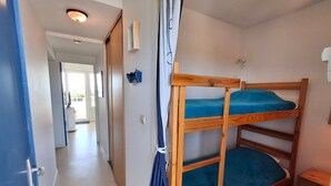 Ein Zimmer mit Etagenbetten, einem kleinen Holzschrank und einer Tür zu einem weiteren Raum.