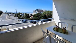 Ein Balkon mit Tisch und Stühlen, der auf eine Straße mit parkenden Autos und ein Gebäude mit blauem Dach blickt.