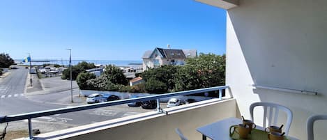 A balcony with a table and chairs, overlooking a street with parked cars and a building with a blue roof.
