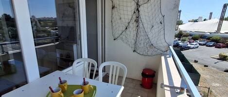 Ein Balkon mit Tisch, gelben Tassen, einer grünen Tablett, weißen Stühlen und einem roten Mülleimer.