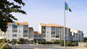 Ein mehrgeschossiges Wohngebäude mit Balkonen, einer Fahnenstange und einer Flagge sowie einem klaren Himmel.