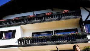 Un edificio de dos pisos con balcones, una bicicleta y una persona leyendo un libro.