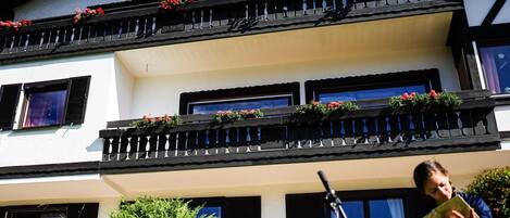 A two-story building with balconies, a bicycle, and a person reading a book.
