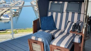 A balcony with a striped sofa, a blue pillow, and binoculars on a wooden table. - 5 Star Holiday Home in Wendtorf (Wendtorf)