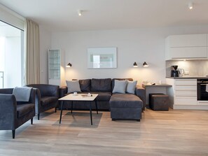 A modern living room with a sofa, a coffee table, and a kitchen area with a coffee machine.