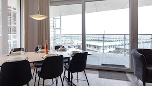 A modern dining room with a large table, black chairs, and a view of a marina through floor-to-ceiling windows.
