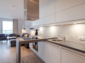 Cozinha moderna com eletrodomésticos integrados, sala de jantar com vista e área de estar com sofá e mesa de centro.