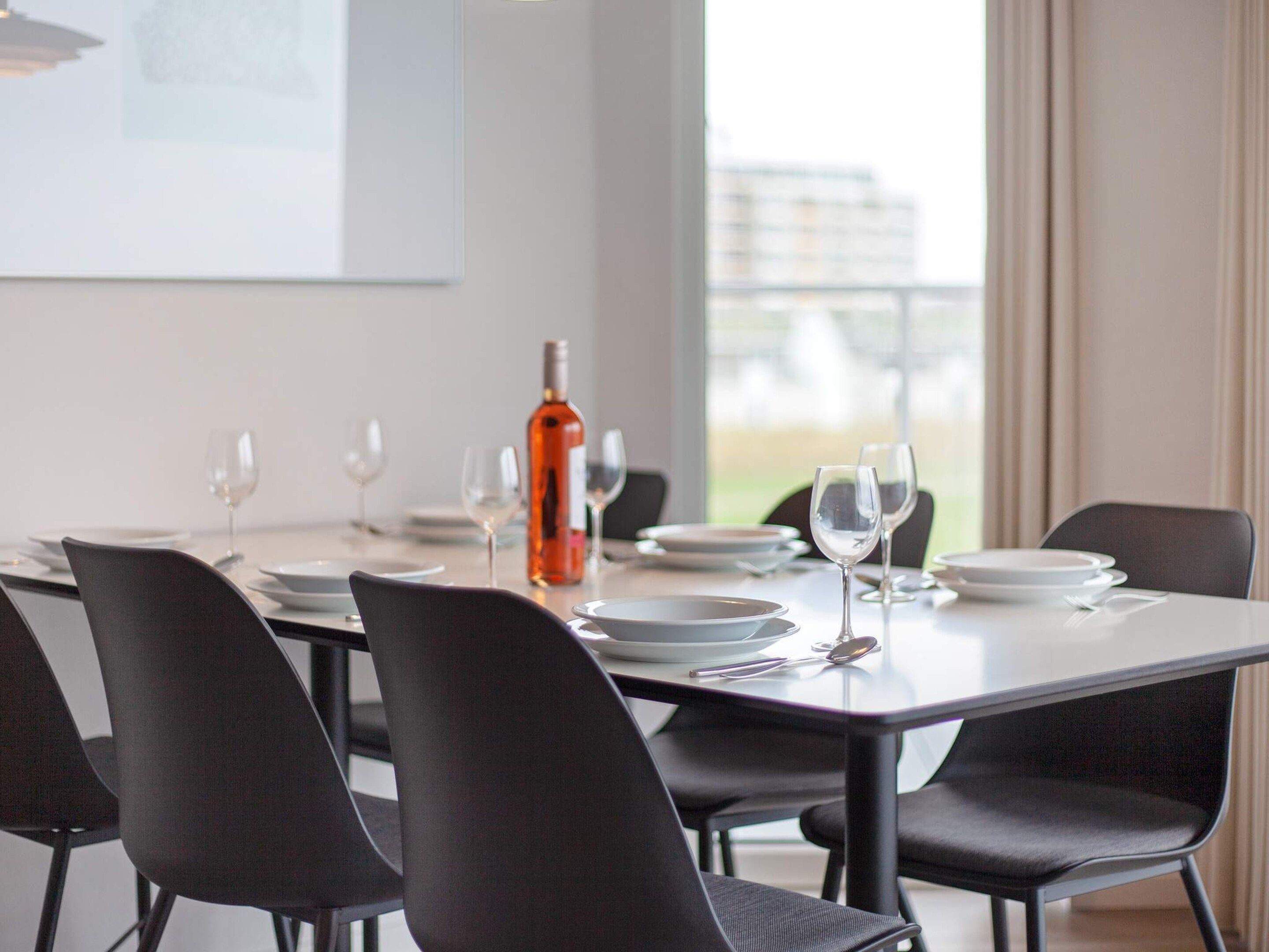 A dining area with a table set for six, including wine glasses and plates, and a bottle of wine.