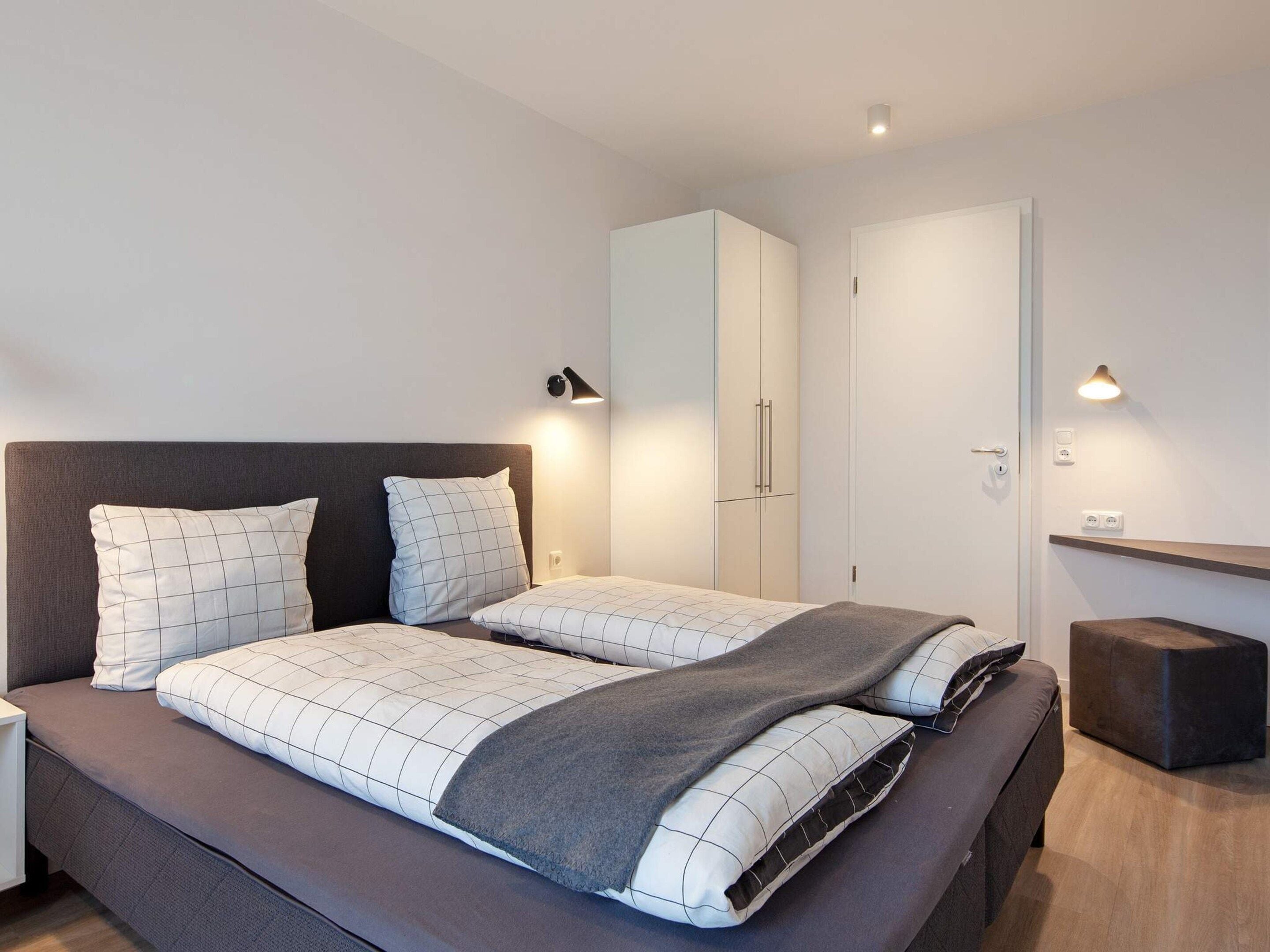 Quarto moderno com uma cama grande, duas mesas de cabeceira, um guarda-roupa e iluminação embutida na parede.