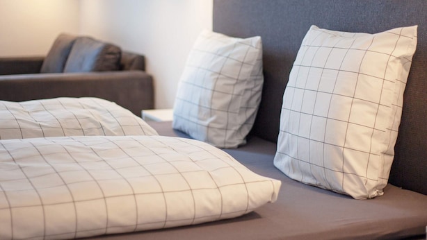 A modern bedroom with a grey headboard, a sofa, and a bed with white pillows featuring a grid pattern.