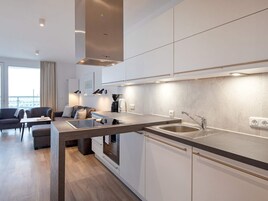 Una cocina moderna con horno empotrado, lavamanos y zona de comedor con mesa y sillas.