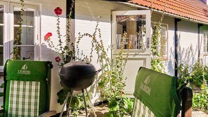 Un patio con una parrilla, dos sillas verdes y una casa blanca de techo rojo.