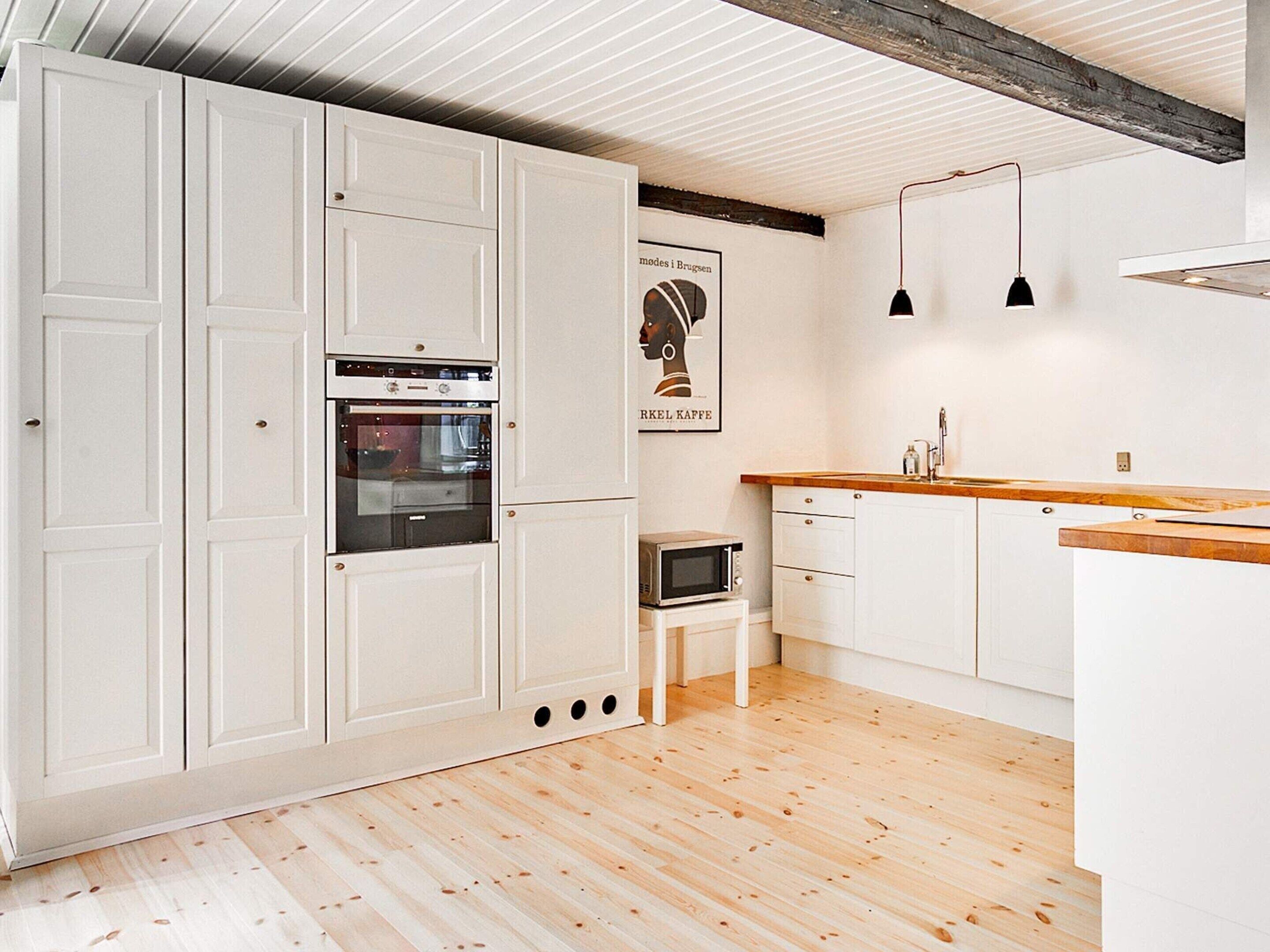 A modern kitchen with white cabinetry, a wooden countertop, and a built-in oven.