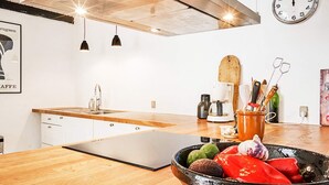 Una cocina moderna con armarios blancos, encimera de madera, cafetera y un bol de verduras.